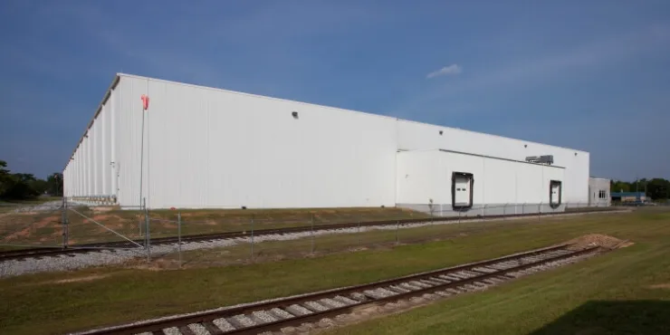 Vista lateral exterior del almacén frigorífico de Lineageen Macon, Atlanta, Georgia, con un almacén blanco, vías de tren adyacentes y un primer plano cubierto de hierba.