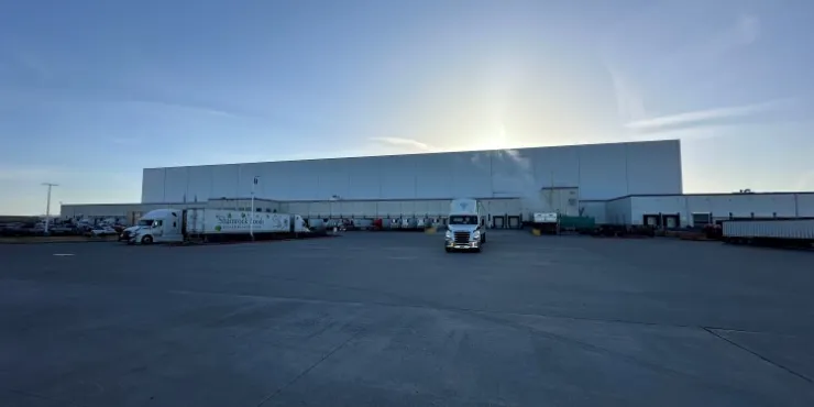Amplia vista del almacén frigorífico de Lineage en Pasco, Washington, con muelles de carga, camiones aparcados y un gran terreno pavimentado al amanecer, que pone de relieve la amplia capacidad logística.