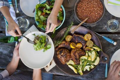 meal on a table with hands passing a dish