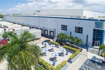 Aerial view of Lineage Logistics cold storage facility in Miami showcasing the expansive warehouse, loading docks with trucks, and the landscaped outdoor area with shaded seating.