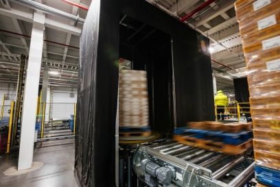 A neatly stacked pallet positioned on a Lineage Eye conveyor system in a clean, well-organized, automated cold storage warehouse, with safety guardrails and scanning stations in the vicinity.