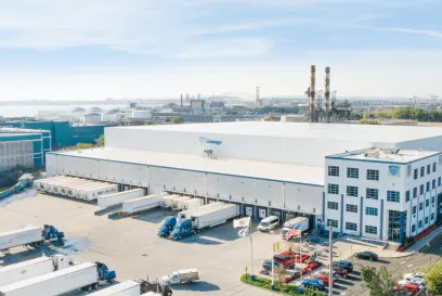 A large Lineage cold storage warehouse in New Jersey, with the Lineage logo, featuring multiple loading docks with trucks, located in an industrial area with proximity to a port.