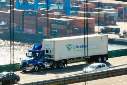 A Lineage truck crossing a bridge with a port full of shipping containers in the background, representing supply chain solutions for navigating tariffs and global trade challenges.