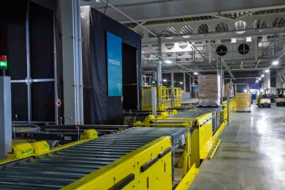 A modern cold storage warehouse featuring yellow conveyor systems and forklifts moving pallets. Lineage Eye automation streamlines receiving and inventory management.