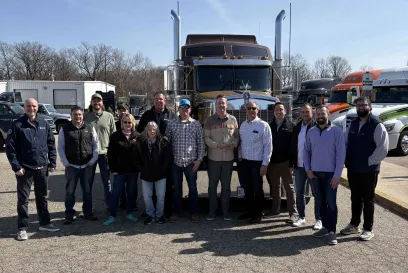 A group of people stand next to a semi truck trailer after accepting an award from Lineage
