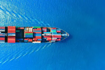 Aerial view of a large cargo ship carrying multicolored shipping containers across a bright blue ocean, symbolizing global trade and port logistics.