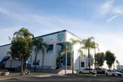 Exterior view of a Lineage Logistics cold storage facility in Southern California, with palm trees, parked vehicles, and clear blue skies.