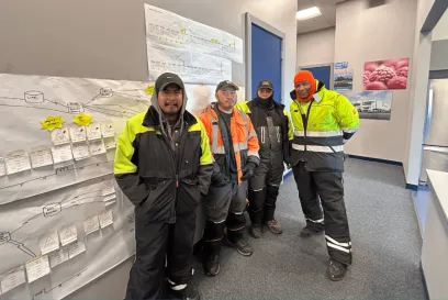 Four Lineage team members at the Dallas Dynasty facility stand proudly in front of a Kaizen event process map, showcasing their continuous improvement efforts.