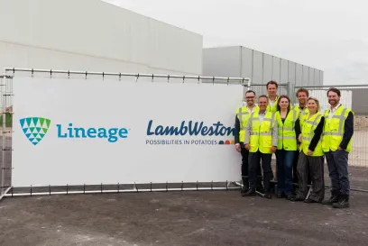 A group of people in high visibility gear stand near a sign announcing Lineage's expansion with customer Lamb Weston