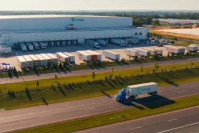 Lineage semi-truck driving past a cold storage facility with multiple docked trailers, representing an integrated cold chain logistics network.