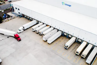 Vista aérea de camiones frigoríficos cargando y descargando en un almacén Lineage , mostrando las operaciones de distribución de servicios alimentarios y cadena de frío.