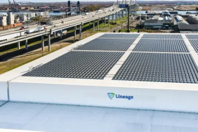 Vista aérea de un almacén frigorífico de Lineage en el noreste de EE.UU. con paneles solares en el tejado, con autopistas cercanas e infraestructuras portuarias visibles al fondo.