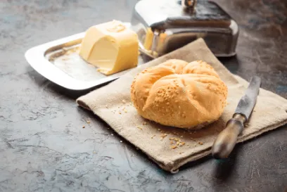 Fresh baked bread roll on a cloth with a knife and a dish of butter on a rustic kitchen surface