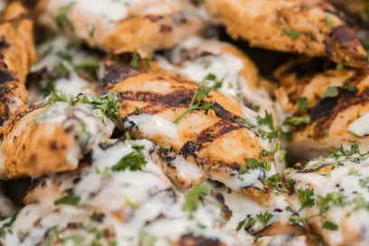 Grilled chicken pieces topped with creamy sauce and herbs, close-up of cooked poultry ready to serve