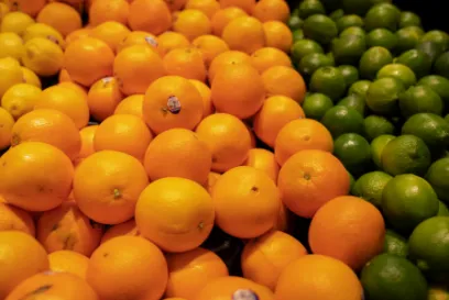 Pile of fresh oranges and green citrus fruit displayed side by side in a produce section