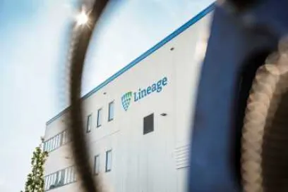 An exterior view of Lineage's cold storage warehouse in Bremerhaven, Germany. The building is white with Lineage's logo and blue and green accents on the outside.