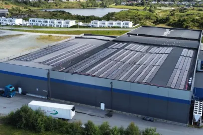 Aerial view of the Lineage cold storage facility in Haugesund, Norway, featuring rooftop solar panels, loading areas and surrounding residential and natural landscapes.