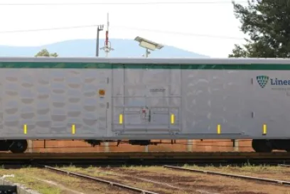 Side view of a silver Lineage LINX insulated railcar sitting on railroad tracks, featuring the Lineage logo and reflective safety markings, with trees and mountains visible in the background.