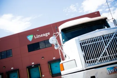 Lineage refrigerated truck parked outside a Lineage cold storage warehouse facility with loading dock doors and company signage visible.
