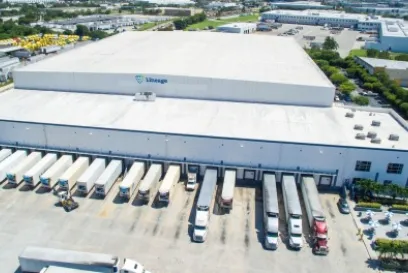 Aerial view of a Lineage cold storage warehouse with refrigerated trucks and trailers positioned at loading docks.