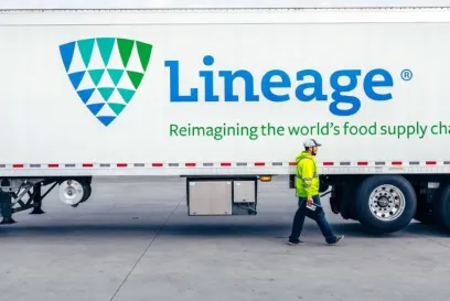 Lineage Une remorque frigorifique est stationnée dans un entrepôt, un employé marchant à côté, illustrant les opérations de transport et de logistique à température contrôlée.