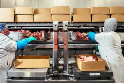 Worker handling boxed food products on a conveyor line inside a Lineage food processing facility.