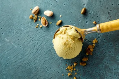 Una bola de helado de pistacho con pistachos picados sobre una superficie azul.