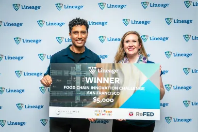 A man and woman hold a large sign declaring them the winners of Lineage's Food Chain Innovation Challenge