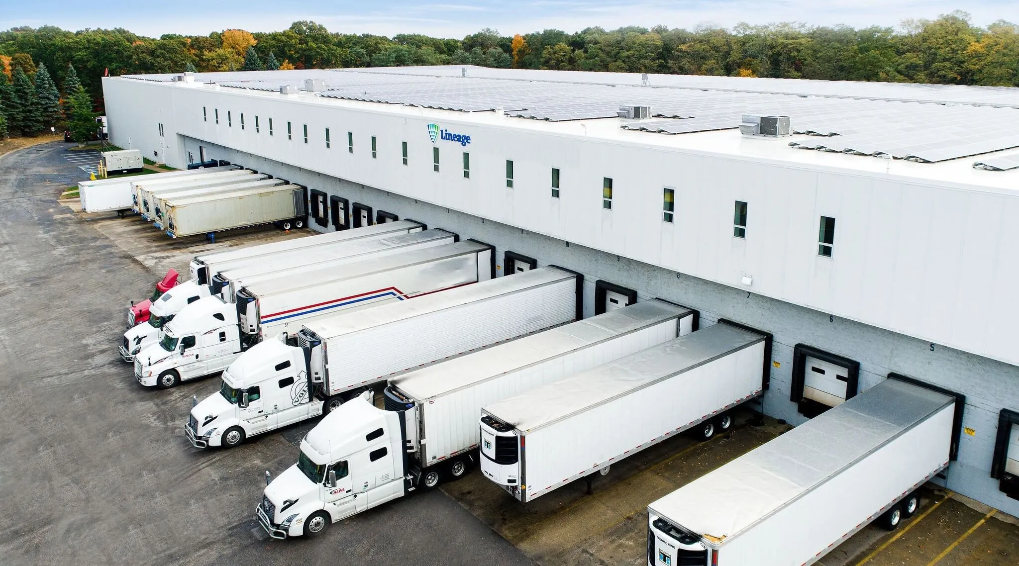 Aerial view of refrigerated trailers parked at loading docks outside a Lineage cold storage facility, illustrating integrated transportation and warehousing operations.