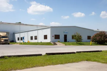 Vista exterior del almacén frigorífico de Lineageen Unadilla, cerca de Atlanta, Georgia, con un almacén blanco con una pequeña entrada de oficina, un camión aparcado y vegetación alrededor.