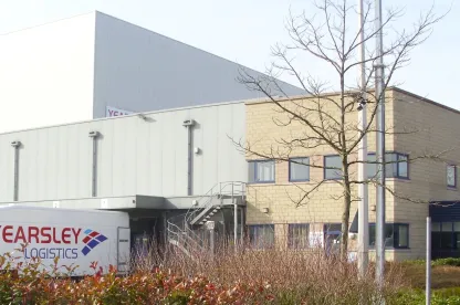 Vista frontal del almacén frigorífico automatizado Hams Hall de Lineageen Coleshill (Reino Unido), con un camión de Yearsley Logistics y una señal de punto de reunión contra incendios.