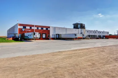 Vista exterior del almacén frigorífico de Lineage en Friona, Texas, con el almacén de ladrillo y blanco, los muelles de carga y los remolques bajo un cielo despejado.