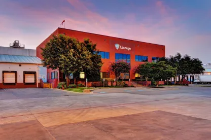 Extérieur de la Lineage à Fort Worth, Texas, avec le bâtiment de bureaux rouge, les quais de chargement et les arbres environnants au crépuscule.