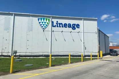 Vue extérieure de Lineagede la Houston Hwy 225, montrant le mur blanc de l’entrepôt avec le Lineage logo, bornes de sécurité jaunes et un ciel bleu clair.