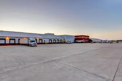 Wide view of Lineage’s McAllen South Ware facility, showing the loading docks, trucks and the red office building at dusk.