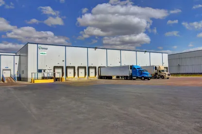 Extérieur de Lineagede l’installation militaire McAllen West, montrant l’entrepôt blanc avec plusieurs quais de chargement et plusieurs camions stationnés sous un ciel partiellement nuageux.