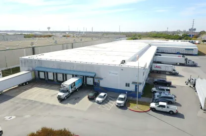 Vue aérienne de LineageSan Antonio Frost Bank Center, montrant l’entrepôt blanc, les quais de chargement, les remorques et les véhicules stationnés par une journée claire.