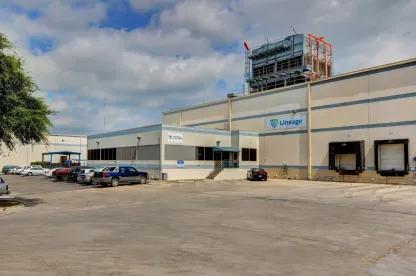 Vue extérieure de LineageSan Antonio Profit, montrant l’entrepôt clair, les quais de chargement et les véhicules stationnés sous un ciel partiellement nuageux.
